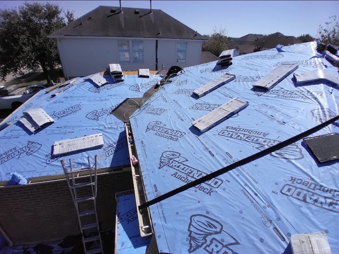 Roof deck with synthetic underlayment and shingle bundles staged for installation